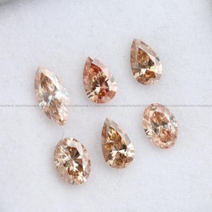 May include: Six loose faceted gemstones in shades of champagne and light brown. The collection includes one marquise cut, two pear cuts, and three oval cut stones, all displaying intricate internal light reflections and a polished, brilliant finish.