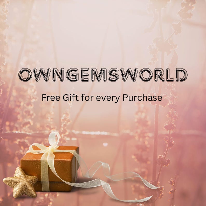 Op de afbeelding: Een bruine geschenkdoos met een gouden ster en lint op een roze achtergrond. De doos is vastgebonden met een gouden lint. De tekst "OWNGEMSWORLD" en "Free Gift for every Purchase" worden weergegeven.