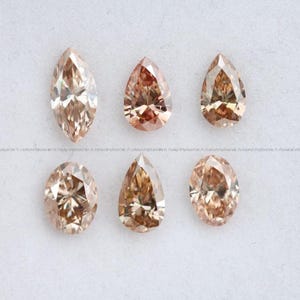 May include: Six loose faceted gemstones in shades of champagne and light brown. The collection includes one marquise cut, two pear shapes, two oval cuts, and one additional pear shape, all featuring intricate geometric facets that reflect light.