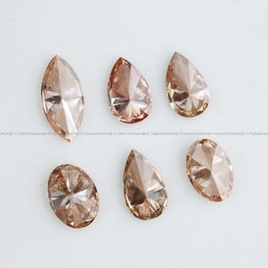 May include: Six loose faceted gemstones in shades of light brown and champagne. The collection includes one marquise cut, two pear shapes, two oval cuts, and one additional pear shape, all featuring intricate geometric facets that reflect light.