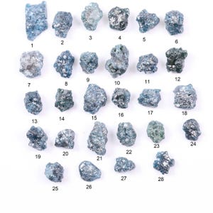 May include: A collection of twenty-eight raw, uncut, blue-grey diamonds, each with a unique, irregular shape. The gemstones are numbered 1 through 28, displayed against a white background. The rough texture and varying shades of blue are visible.
