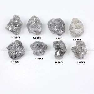Puede incluir: Ocho diamantes grises en bruto y sin tallar dispuestos en dos filas. Cada piedra presenta una forma cristalina irregular y única con una superficie texturizada. Los pesos están etiquetados como 1.29Ct, 1.68Ct, 1.74Ct, 1.53Ct, 1.19Ct, 1.15Ct, 0.96Ct y 1.60Ct.