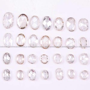 May include: A collection of twenty-eight loose, oval-shaped, rose-cut clear gemstones arranged in four horizontal rows. Each stone features a faceted surface with a flat base and a pointed top, displaying a translucent, colourless appearance.