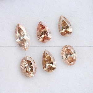 May include: A collection of five loose faceted gemstones in shades of champagne and light brown. The stones feature various cuts, including marquise, pear, and oval shapes, each displaying intricate geometric facets that reflect light across the surface.