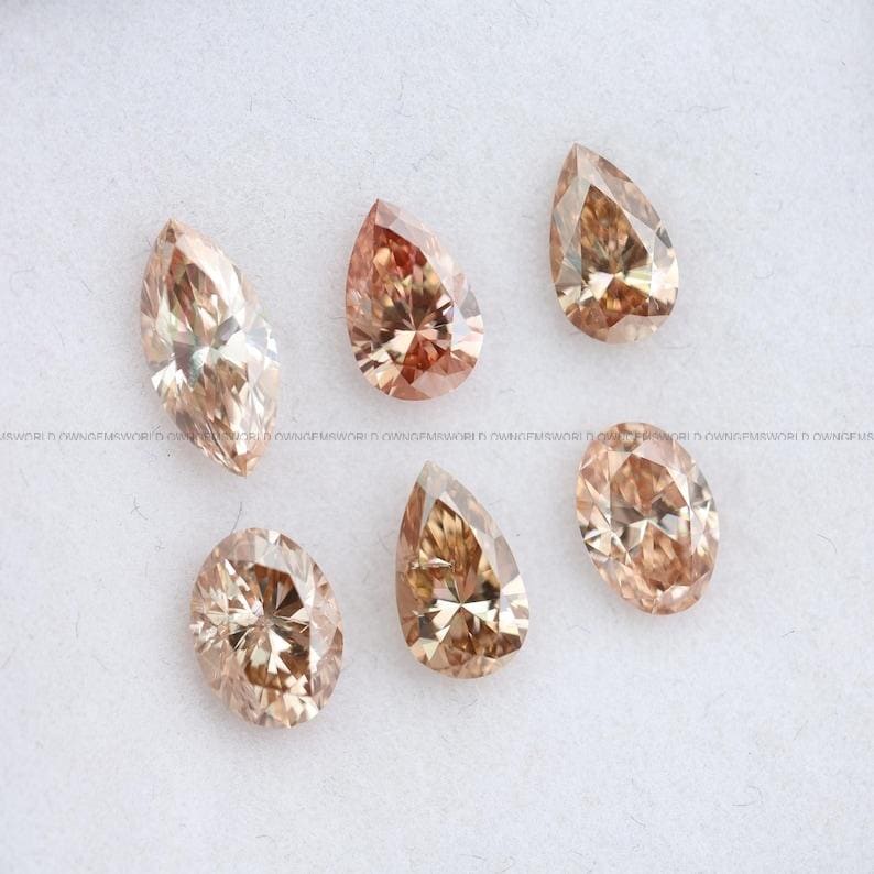 May include: A collection of five loose faceted gemstones in shades of champagne and light brown. The stones feature various cuts, including marquise, pear, and oval shapes, each displaying intricate geometric facets that reflect light across the surface.