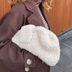 May include: A brown wool coat with a large, fluffy white faux fur clutch. The coat has a button closure and a collar.