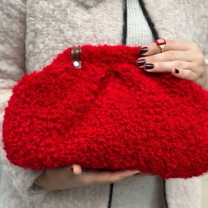 May include: A bright red fluffy clutch purse with a brown leather strap.