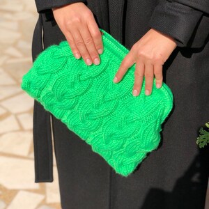 May include: A bright green knitted clutch bag with a cable knit pattern.