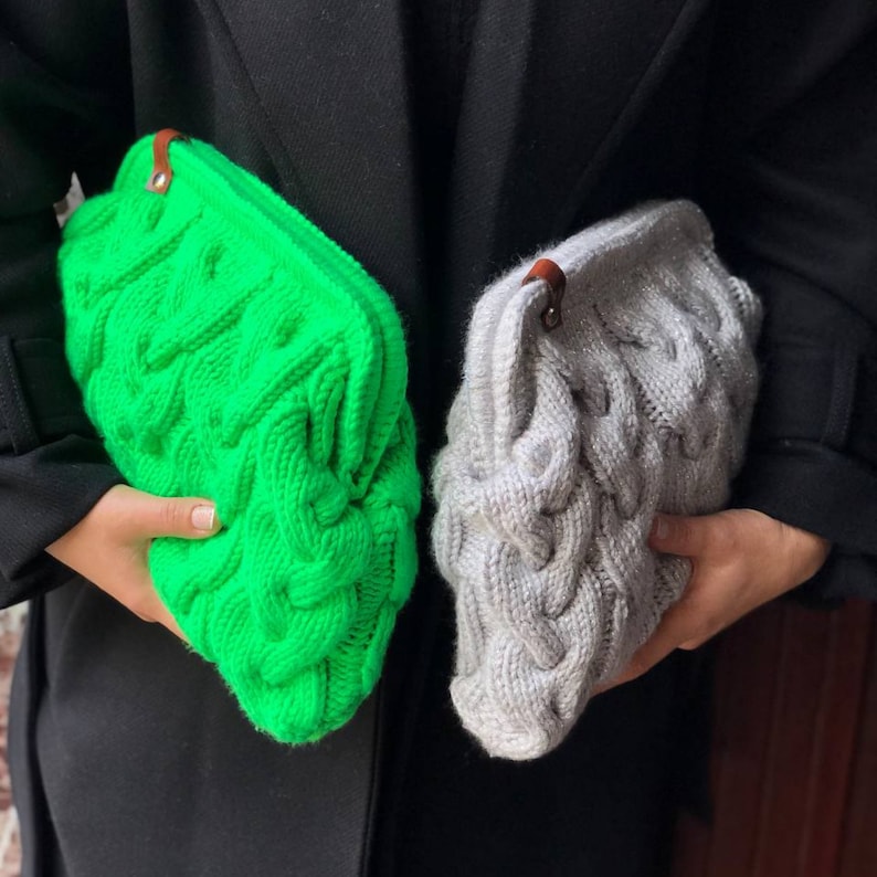 May include: Two knitted clutches, one green and one gray, with a cable knit pattern. The clutches have brown leather handles.
