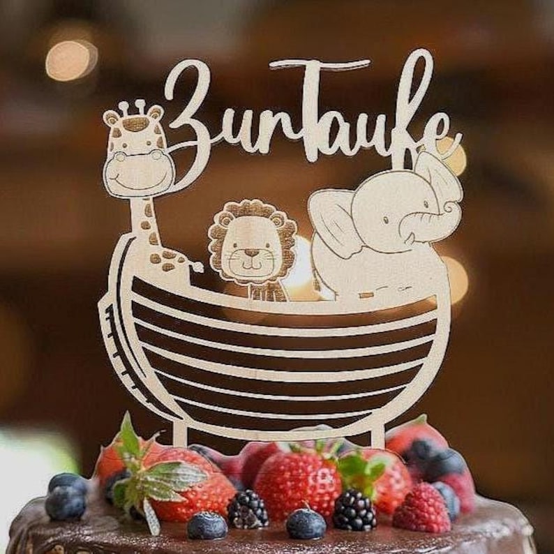 Pu&ograve; includere: Topper per torta in legno con il testo tedesco "Zur Taufe" (Battesimo). Il topper presenta una giraffa, un leone e un elefante in una barca. La torta &egrave; decorata con fragole fresche, mirtilli e more.