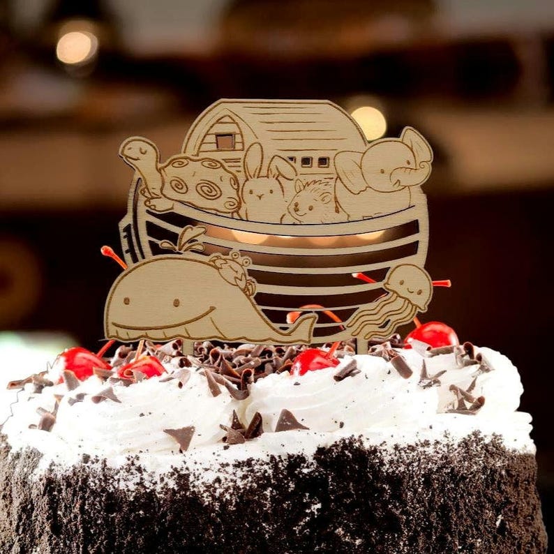 Pu&ograve; includere: Topper per torta in legno raffigurante l'Arca di No&egrave; con animali: una tartaruga, un coniglio, un riccio e un elefante. Sono inclusi anche una balena e una medusa. Il topper &egrave; posto su una torta con glassa bianca, scaglie di cioccolato e ciliegie.