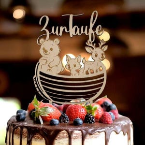 Pu&ograve; includere: Topper per torta in legno con la scritta tedesca "Zur Taufe" sopra una barca con un orso, una volpe e un cervo. La torta &egrave; guarnita con fragole fresche, mirtilli e more, e ricoperta di ganache al cioccolato.