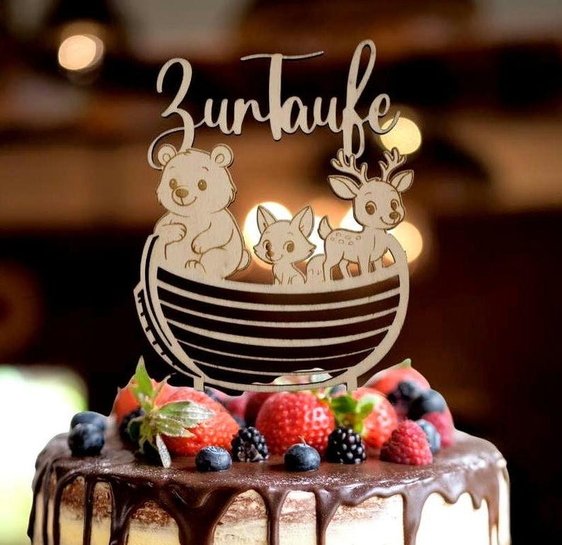 Pu&ograve; includere: Topper per torta in legno con la scritta tedesca "Zur Taufe" sopra una barca con un orso, una volpe e un cervo. La torta &egrave; guarnita con fragole fresche, mirtilli e more, e ricoperta di ganache al cioccolato.