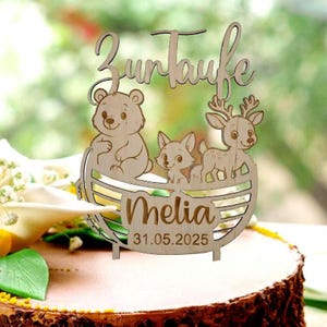 Pu&ograve; includere: Topper per torta in legno con le parole "Zur Taufe" e il nome "Melia" con la data 31.05.2025. Il topper presenta un orso, una volpe e un cervo in una barca di legno.