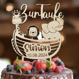 Könnte beinhalten: Kuchenaufsatz aus Holz mit der Aufschrift "Zur Taufe" und einem Design mit Giraffe, Löwe und Elefant. Der Name "Simon" und das Datum "10.08.2024" sind ebenfalls enthalten. Der Kuchen ist mit Erdbeeren, Blaubeeren und Brombeeren belegt.