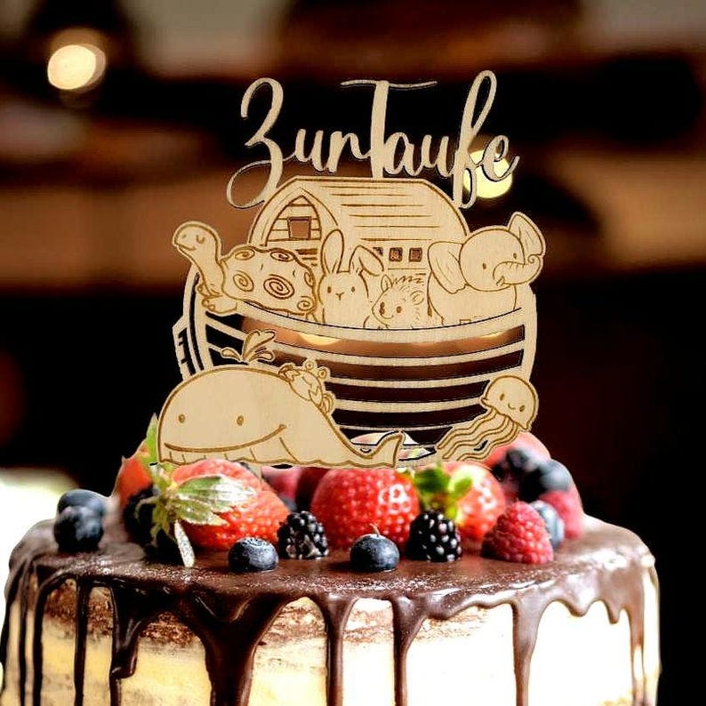 Pu&ograve; includere: Un cake topper in legno con il testo tedesco "Zur Taufe" (Per il battesimo) presenta un'arca con figure di animali. La torta &egrave; decorata con frutti di bosco freschi e ganache al cioccolato.