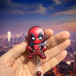 May include: A red and black glitter Deadpool character badge reel with a red glitter button. The reel is attached to a clear plastic retractable cord.