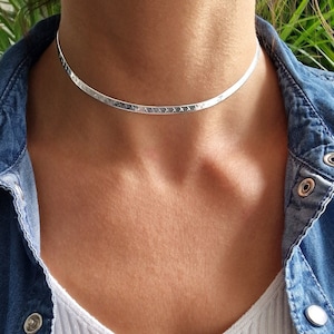 Könnte beinhalten: Eine silberne Choker-Kette mit gehämmerter Oberfläche. Die Kette ist dünn und zart und wird von einer Person mit hellem Teint getragen.