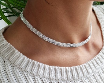 Puede incluir: Un collar gargantilla trenzado de plata en el cuello de una persona. El collar es un diseño simple y delicado.