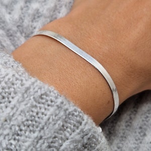 Op de afbeelding: Een zilveren slangenketting armband om de pols van een persoon.