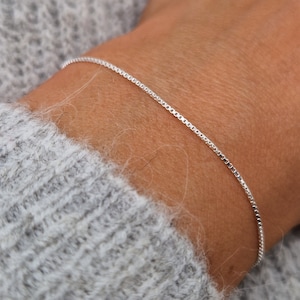 Könnte beinhalten: Ein silbernes Kettenarmband am Handgelenk einer Person.