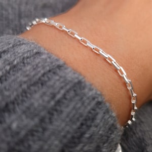 Könnte beinhalten: Ein silbernes Kettenarmband mit einem Gliederketten-Design. Das Armband befindet sich an einem Handgelenk.