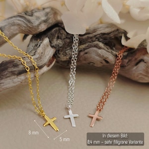 May include: Three delicate necklaces featuring small cross pendants in gold, silver, and rose gold tones. Each cross measures 8 mm in height and 5 mm in width. The chains are 0.4 mm thick. The pendants are displayed against a piece of driftwood.