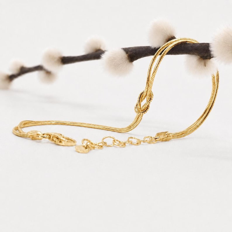 Puede incluir: Una pulsera de cadena de serpiente en tono dorado con un detalle de nudo central. La pulsera incluye un cierre de mosquet&oacute;n y una cadena extensora ajustable con peque&ntilde;os eslabones circulares para un ajuste flexible en la mu&ntilde;eca.
