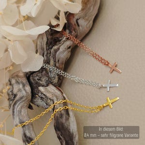 May include: Three delicate necklaces featuring small cross pendants in rose gold, silver, and gold tones. Each necklace has a fine chain and a cross charm. A text box in the image states 0.4 mm - sehr filigrane Variante.