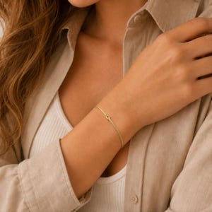 Puede incluir: Una pulsera de cadena fina de oro con un peque&ntilde;o detalle de nudo centrado. La delicada banda met&aacute;lica descansa sobre la piel, mostrando un acabado pulido simple con un solo bucle central que forma un dise&ntilde;o de nudo en la cadena delgada.