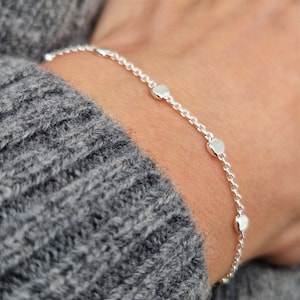 May include: A silver chain bracelet with small, round, textured charms. The bracelet is on a person's wrist.