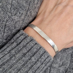 Könnte beinhalten: Ein silbernes Kettenarmband mit einem Fischgrätenmuster.