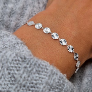 May include: A silver bracelet with a chain made of small, round, textured discs.
