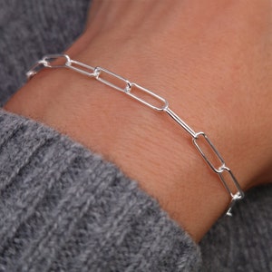 Könnte beinhalten: Ein silbernes Kettenarmband mit einem einfachen, verlinkten Design. Das Armband besteht aus ovalen Gliedern.