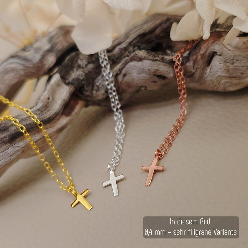 May include: Three delicate necklaces featuring small cross pendants in gold, silver, and rose gold tones. Each necklace has a fine chain and a minimalist cross charm. The text in the image indicates a 0.4 mm filigree variant for these items.