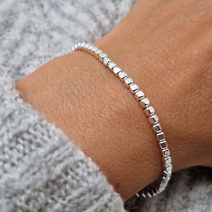 May include: A silver bracelet with small, square-shaped beads.