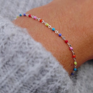 Könnte beinhalten: Ein silbernes Kettenarmband mit bunten Perlen. Die Perlen sind in einem Regenbogenmuster angeordnet, mit roten, orangefarbenen, gelben, grünen, blauen, indigofarbenen und violetten Perlen.