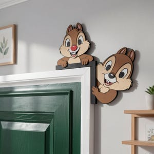 May include: Two wooden Chip and Dale figures, with brown fur, tan faces, and red noses, are attached to a door frame. The figures are smiling and peeking out from the frame, adding a playful touch to the decor.