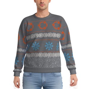 May include: Gray crew neck sweater with a festive pattern. The design includes orange circles, white lace-like patterns, blue snowflakes, and orange stripes. The sweater has ribbed cuffs and hem.
