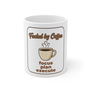 May include: A white ceramic mug featuring a brown graphic design with the text "Fueled by Coffee" at the top and "focus plan execute" at the bottom. In the center, there is an illustration of a steaming cup of coffee in shades of brown.
