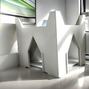 Puede incluir: Una casa para perros moderna de color blanco con dos entradas. La casa está hecha de madera y tiene un diseño simple y geométrico.