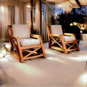 Könnte beinhalten: Zwei Holzstühle mit weißen Kissen stehen auf einer gefliesten Terrasse. Die Stühle haben ein schlichtes, modernes Design mit einem Kreuzmuster auf der Rückenlehne.