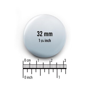 May include: A white round button with the text "32 mm 1 1/4 inch" printed in black.