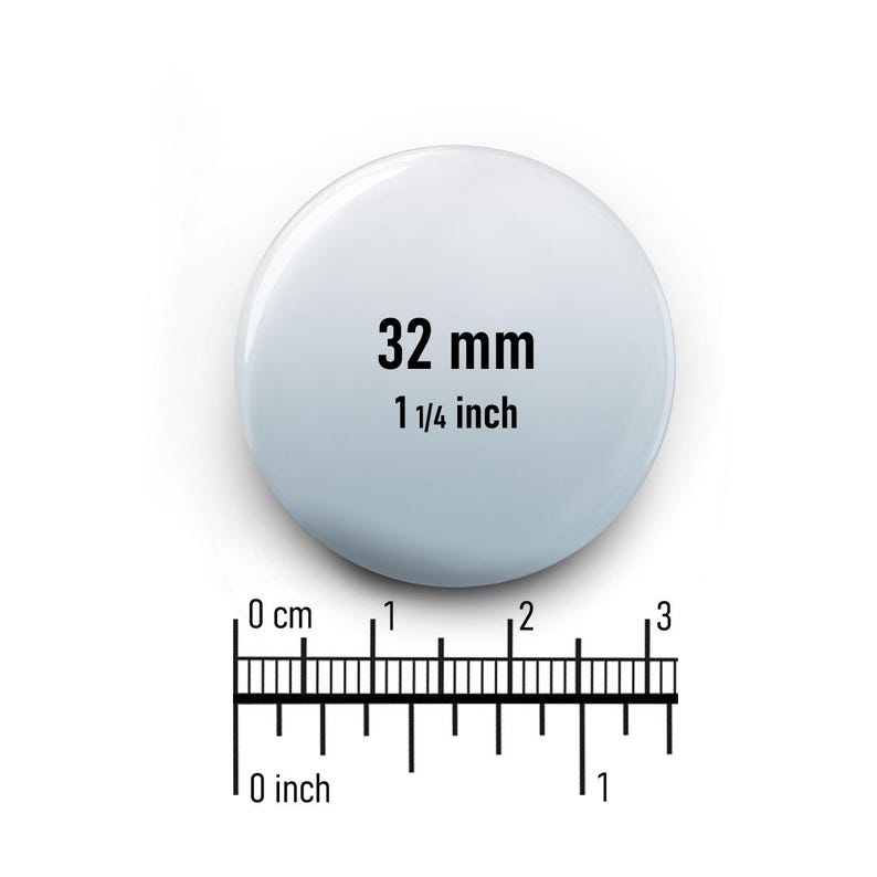 May include: A white round button with the text "32 mm 1 1/4 inch" printed in black.