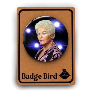 May include: A round button badge featuring a woman with white hair and a pink and black patterned shirt. The background is blue with white lights. The text "Badge Bird" is printed below the badge.
