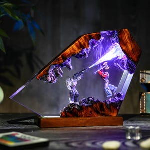 May include: A unique resin lamp featuring a battle scene with two action figures. The lamp has a wooden base and frame with a clear resin center. The figures are illuminated with purple and white light, creating a dramatic effect.
