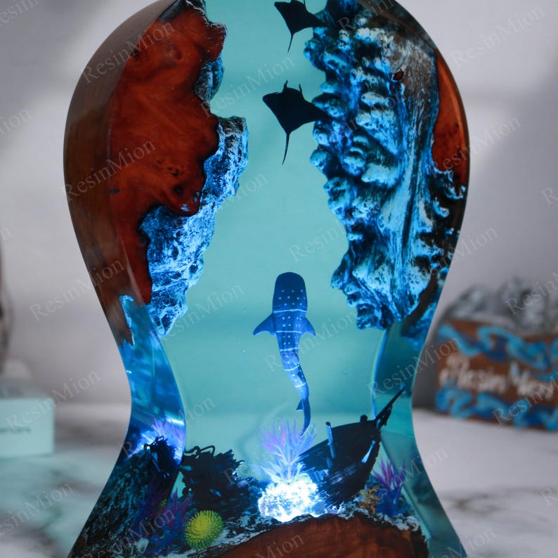 May include: A wooden base with a clear resin casting of a whale shark swimming in a blue ocean scene. The resin casting includes coral, a sunken ship, and smaller fish. The base is lit from below with a blue light.