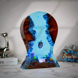 May include: A resin sculpture of a turtle swimming in a blue and turquoise ocean. The sculpture is made of wood and resin and has a light blue glow. The turtle is surrounded by coral and other sea life.