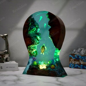 May include: A resin sculpture depicting a turtle swimming in a blue and green ocean scene. The sculpture is illuminated from within, creating a glowing effect. The sculpture is crafted from resin and wood, making it a unique and beautiful piece of art.