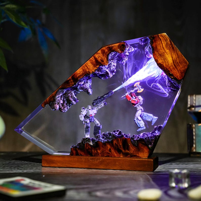 May include: A unique resin lamp featuring a battle scene with two action figures. The lamp has a wooden base and frame with a clear resin center. The figures are illuminated with a blue light, creating a dramatic effect. The lamp is a decorative item.